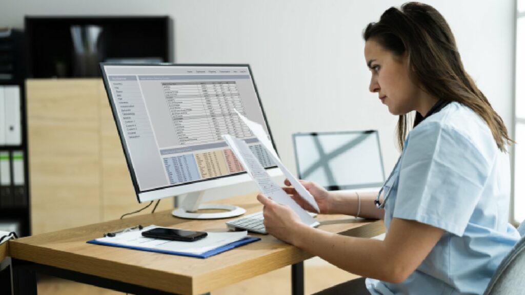 Nurse sitting at desk in front of a computer reading notes