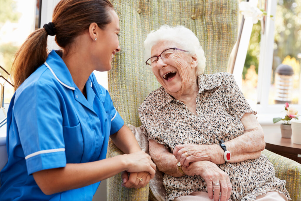 Community Nursing: Senior Woman and a Community Nurse Sitting in Chair and Laughing in Retirement Home